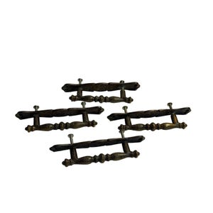 May include: A set of four antique brass-toned metal drawer pulls. Each pull features a decorative, elongated backplate with scalloped edges and a central handle bar with a spindle-like design, complete with two silver-toned mounting screws attached.