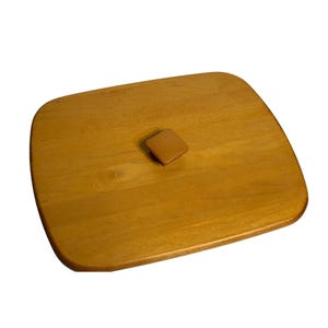 May include: A light brown, rectangular wooden lid with rounded corners and a small, square handle. The lid has a smooth, polished finish and appears to be made of a single piece of wood. The handle is also made of wood and is the same color as the lid.