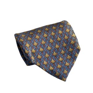 May include: A folded necktie with a repeating pattern of gold and orange fan-like shapes set within a blue diamond grid. The tie is made of a smooth, possibly silk, material.