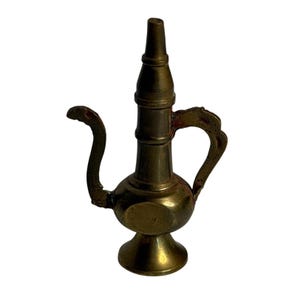 May include: A vintage brass oil lamp with a curved spout and a handle. The lamp has a bulbous body and a tall, slender neck. The brass has a warm, aged patina, suggesting it is an antique.