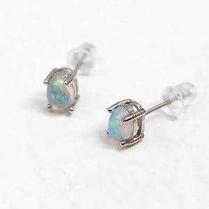 May include: A pair of stud earrings featuring oval-shaped opals set in silver-colored metal. The opals display a mix of pastel colors, including blue, pink, and white. The earrings have a post and backing for secure wear.