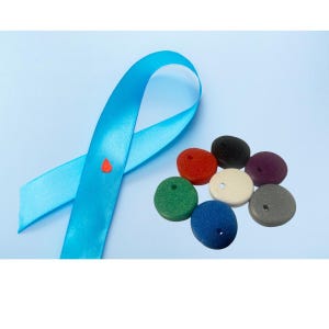 May include: A light blue ribbon with a small orange drop, and a collection of colorful, round, porous objects. The objects are in various colors, including red, black, purple, white, green, blue, and gray. The background is a light blue.