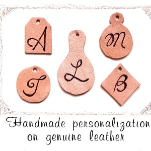 Peut inclure: Gros plan sur cinq étiquettes personnalisées en cuir de couleur marron clair, de formes variées, avec des lettres manuscrites noires. Le texte "Handmade personalization on genuine leather" est visible en dessous.