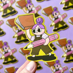 Pode incluir: Um adesivo com um personagem de desenho animado segurando um livro e um grande lápis rosa. O personagem tem cabelo roxo, uma camisa branca e um macacão marrom. O adesivo está em um fundo amarelo.