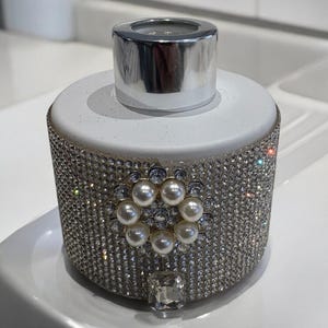 May include: A white ceramic diffuser bottle with a silver lid, covered in sparkling rhinestones and a pearl-like embellishment.