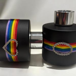 Könnte beinhalten: Zwei schwarze Glasflaschen mit Regenbogenband und Strasssteinen. Die Flaschen haben silberne Verschlüsse und sind mit einer klaren Flüssigkeit gefüllt.