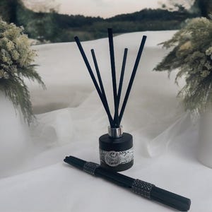 Könnte beinhalten: Schwarze Diffuserflasche mit silbernem Deckel und einem weißen und schwarzen Schlangenhautmuster. Die Flasche hat schwarze Diffuserstäbchen.