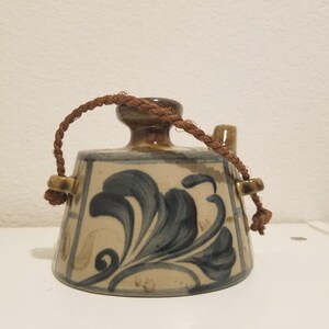May include: A small, brown and white ceramic teapot with a blue floral design. The teapot has a brown rope handle and a spout.