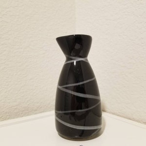 May include: A black ceramic sake bottle with a white swirl design.