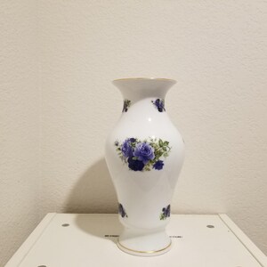 May include: White ceramic vase with a gold rim and blue and white floral design. The vase has a classic shape and is perfect for displaying flowers.