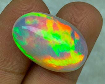 May include: A vibrant, iridescent opal cabochon with a mix of green, orange, and pink hues. The oval-shaped gemstone has a smooth, polished surface.