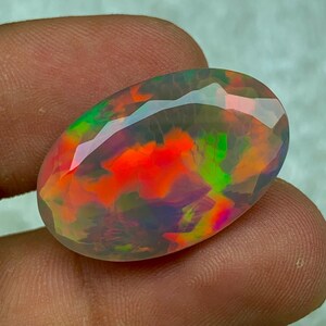 Puede incluir: Una gema de ópalo vibrante y multicolor con una superficie lisa y pulida. El ópalo muestra una gama de colores, incluyendo rojo, naranja, verde y azul.