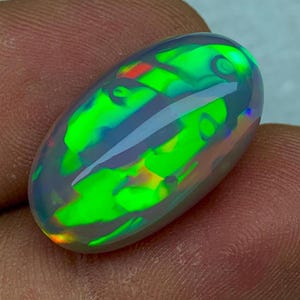 Könnte beinhalten: Ovaler grüner Opal-Edelstein mit schillernden Farbeffekten, darunter Rot, Gelb und Blau.
