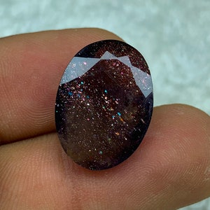 May include: A dark brown oval gemstone with iridescent glitter throughout. The gemstone has a smooth, polished surface.