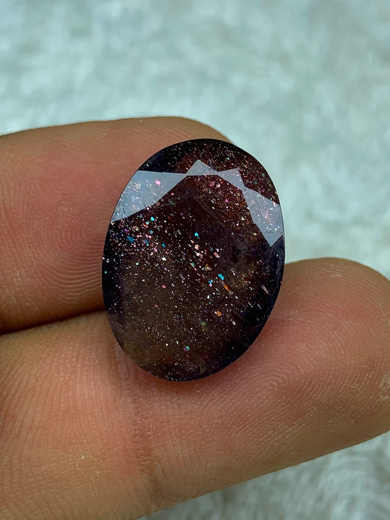 May include: A dark brown oval gemstone with iridescent glitter throughout. The gemstone has a smooth, polished surface.