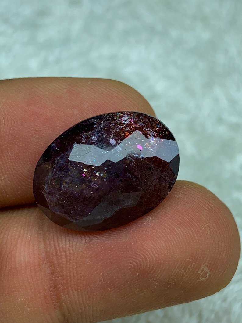 May include: A dark purple oval gemstone with iridescent sparkle and a faceted cut.