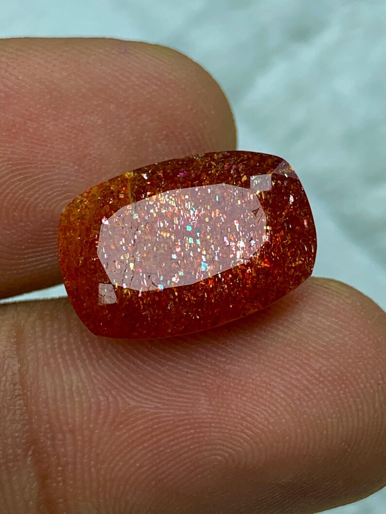 May include: A large, rectangular, orange sunstone gemstone with a shimmering, iridescent finish. The stone has a reddish-brown hue with a subtle sparkle.
