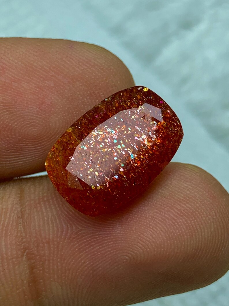 May include: A red, orange and gold sunstone gemstone with a rectangular shape and a sparkly, iridescent finish.