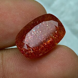 May include: A large, rectangular, red sunstone gemstone with a shimmery, iridescent finish.