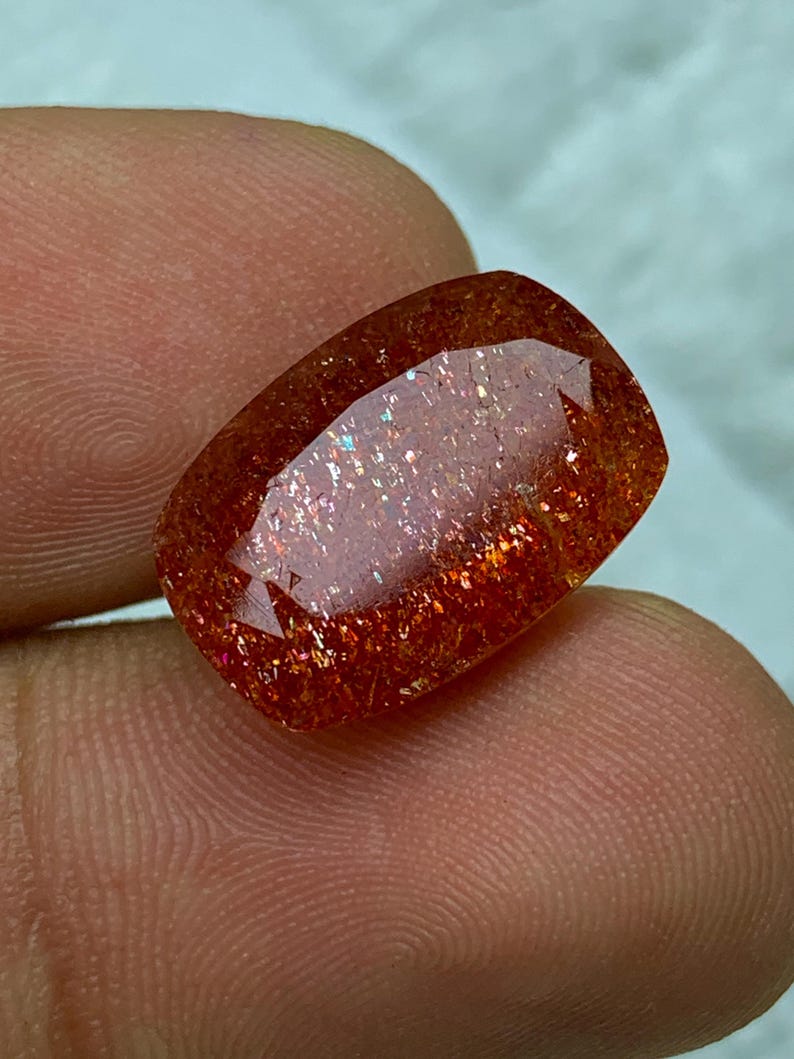 May include: A large, rectangular, red sunstone gemstone with a shimmery, iridescent finish.