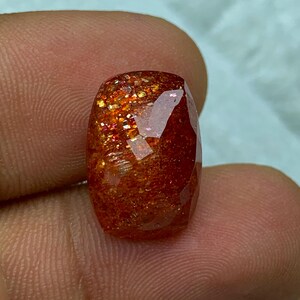 May include: A large, faceted, orange sunstone gemstone with a reddish-brown hue and iridescent sparkle.