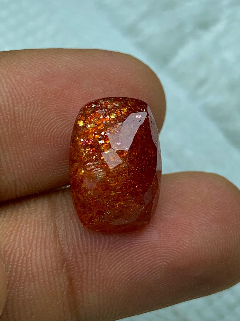 May include: A large, faceted, orange sunstone gemstone with a reddish-brown hue and iridescent sparkle.
