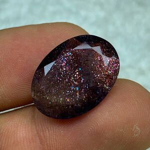 May include: A dark purple oval gemstone with iridescent glitter embedded throughout. The gemstone has a faceted cut.