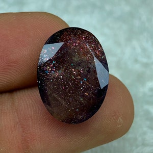 May include: A dark purple oval-shaped gemstone with a sparkly, iridescent finish. The stone has a speckled appearance with flecks of gold, silver, and pink.
