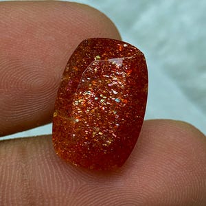 May include: A large, rectangular, red sunstone gemstone with a shimmery, iridescent finish.