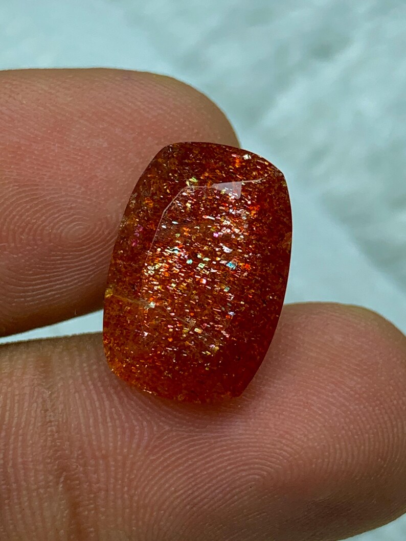 May include: A large, rectangular, red sunstone gemstone with a shimmery, iridescent finish.