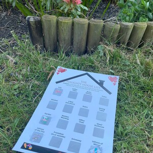 May include: A white paper titled "The Naughty House List" lies on grass. The list includes places like the sofa, bed, and front door. The paper is near a wooden fence and pink flowers.