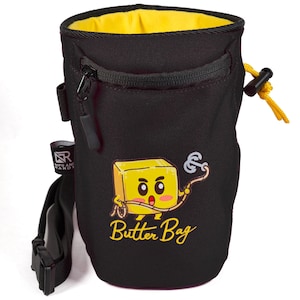 May include: Black climbing chalk bag with a yellow zipper and a yellow cartoon butter character holding a rope. The bag has a small zippered pocket on the front and a yellow drawstring. The text "Butter Bag" is printed on the front of the bag.