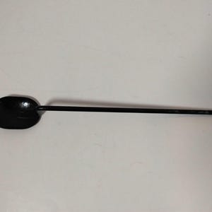 May include: A black metal spoon with a long handle and an oval-shaped bowl. The spoon is designed for cooking or serving. The handle is thin and straight, and the bowl is slightly curved. The spoon is made of a solid, durable material.