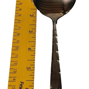 May include: A stainless steel spoon with a rounded bowl and a decorative handle. The spoon is approximately 7 inches long. A yellow ruler with black markings is next to the spoon.