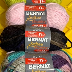 Könnte beinhalten: Vier Knäuel Bernat Softee Chunky Garn in verschiedenen Farben: Limettengrün, Rosa, Braun und Mehrfarbig. Jedes Knäuel hat ein Etikett mit dem Markennamen, dem Garngewicht und der Maschenzahl pro Zoll.