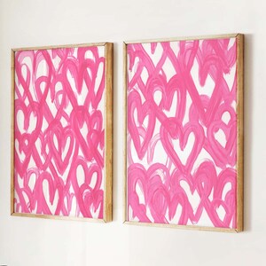 May include: Two framed pink abstract paintings with a white background and a wooden frame. A wicker rocking horse and a wicker chair with a green velvet pillow are in the foreground.