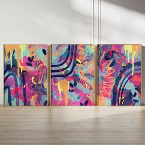 May include: Three abstract paintings in gold frames. The paintings are a mix of pink, purple, blue, yellow, and black. The paintings are all different, but they have a similar style.
