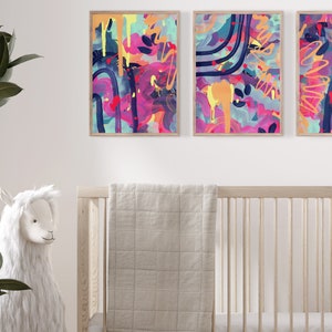 May include: Three abstract paintings in wooden frames with colorful, geometric shapes and splatters of paint in shades of pink, blue, yellow, and green.