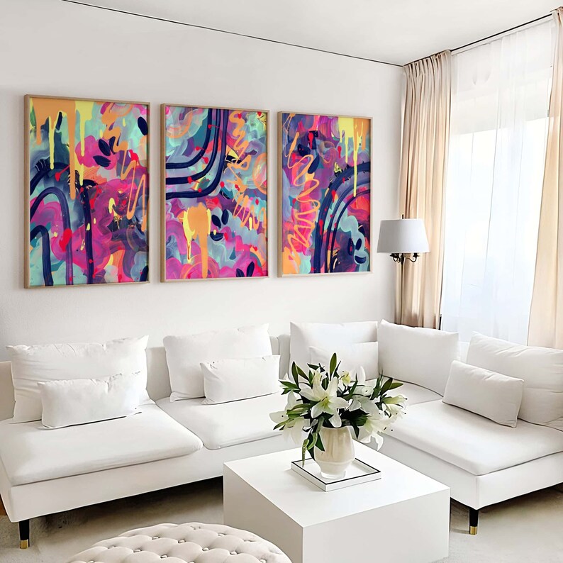 May include: Three abstract paintings with colorful, swirling patterns in shades of pink, blue, yellow, and purple. The paintings are framed in wood and hung on a white wall above a white sectional sofa.