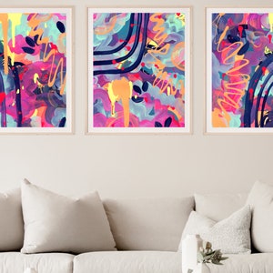 May include: Three abstract paintings in colorful frames. The paintings feature a mix of pink, blue, yellow, and orange colors with abstract shapes and lines.