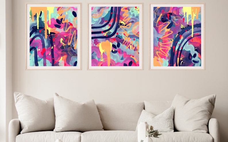 May include: Three abstract paintings in colorful frames. The paintings feature a mix of pink, blue, yellow, and orange colors with abstract shapes and lines.