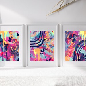 May include: Three framed abstract paintings with a colorful, vibrant, and modern style. The paintings feature a mix of pink, purple, blue, yellow, and orange colors with black lines and shapes.