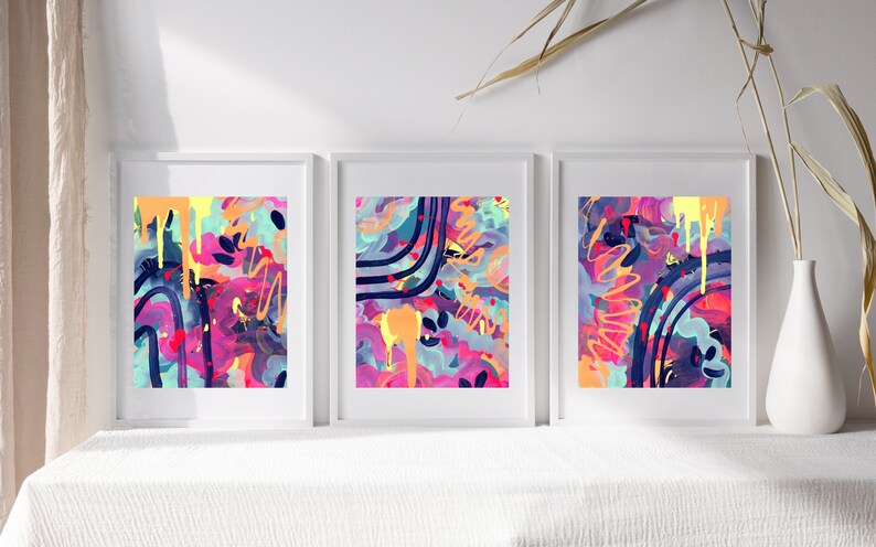 May include: Three framed abstract paintings with a colorful, vibrant, and modern style. The paintings feature a mix of pink, purple, blue, yellow, and orange colors with black lines and shapes.