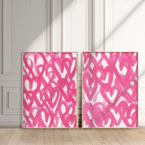 May include: Two framed abstract paintings with pink brushstrokes in the shape of hearts on a white background.