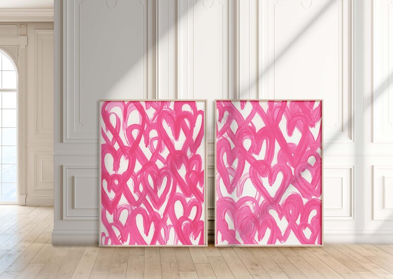May include: Two framed abstract paintings with pink brushstrokes in the shape of hearts on a white background.