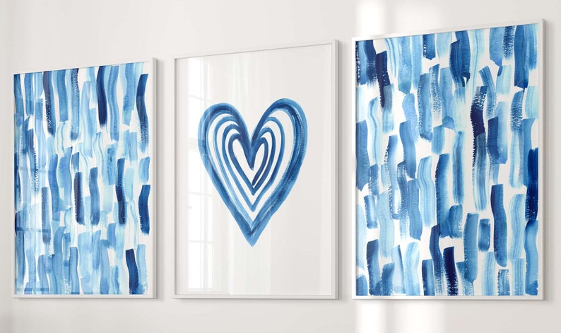 Puede incluir: Conjunto de tres l&aacute;minas enmarcadas. Dos l&aacute;minas muestran pinceladas verticales en tonos azules sobre fondo blanco. La l&aacute;mina central presenta un coraz&oacute;n azul. Los marcos son blancos.
