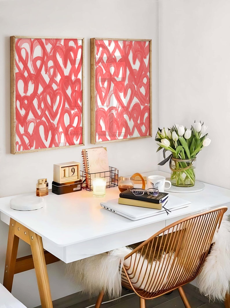 May include: A white desk with a laptop, a stack of books, a white candle, a wooden calendar showing the date 19th, a vase of white tulips, and two framed prints of pink hearts on a white background.