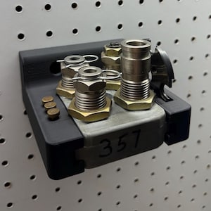 May include: A collection of metal fittings, including threaded connectors and cylindrical components, mounted on a black bracket. The number "357" is visible on the metal plate. Small brass-colored rivets are also present.