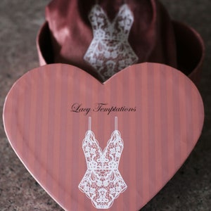 May include: A heart-shaped box with a pink and white striped pattern. The box has a white lace design and the text "Lacy Temptations" printed on the front.