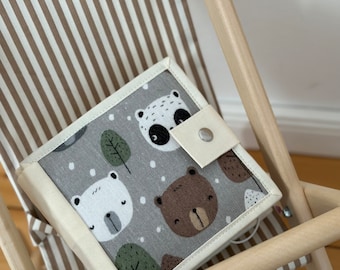 May include: A gray and white fabric book with a white border and a button closure. The book features a repeating pattern of bears, pandas, and trees on a gray background.